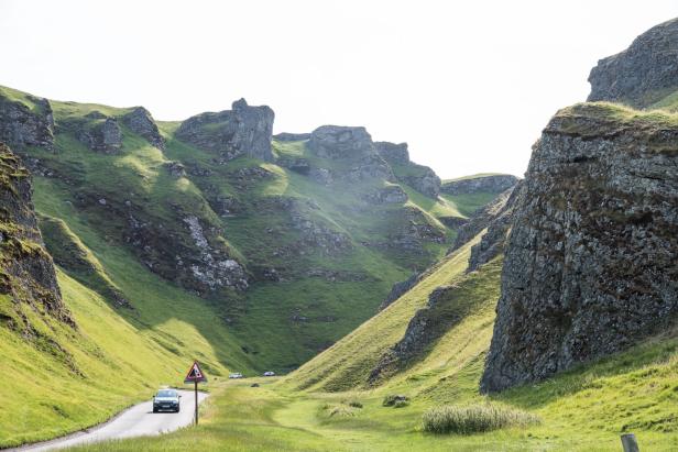 Ein Auto fährt auf einer Straße durch eine grüne Schlucht.
