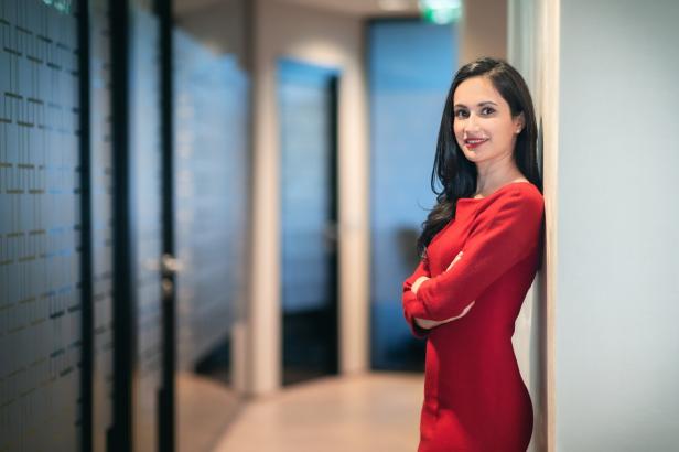 Eine Frau im roten Kleid lehnt an einer Wand in einem Bürogebäude.