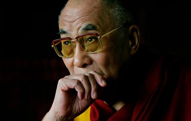 Der Dalai Lama mit Brille, die Hand vor dem Mund.