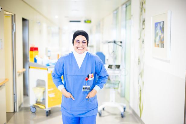 Eine lächelnde Krankenschwester mit Hijab steht in einem Krankenhausflur.