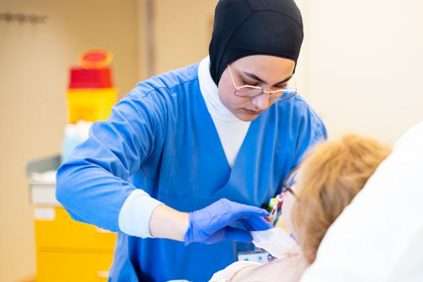 Eine Krankenschwester in blauer Arbeitskleidung versorgt einen Patienten.
