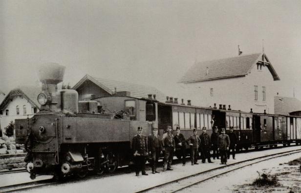 Eine historische Dampflokomotive mit Personal steht auf einem Bahnhof.