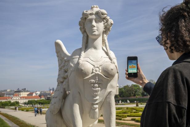 Im Garten des Belvedere steht eine Sphinx-Statue, die von einer Frau fotografiert wird.