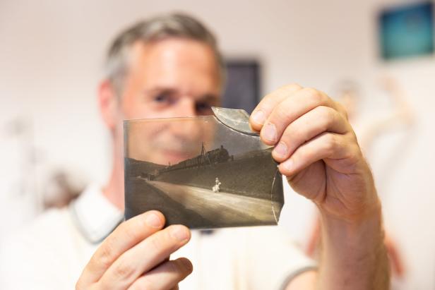 Ein Mann betrachtet ein beschädigtes Schwarzweißfoto einer alten Zugszene.