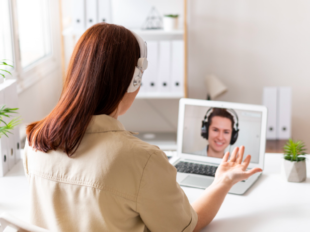 Frau mit roten Haaren und weißen Kopfhörern sitzt vor dem Laptop in einem Videocall