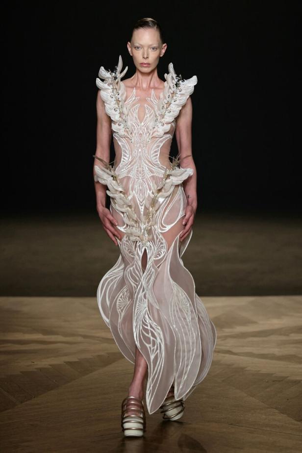 Ein Model präsentiert ein aufwendiges, weißes Kleid von Iris van Herpen auf dem Laufsteg.