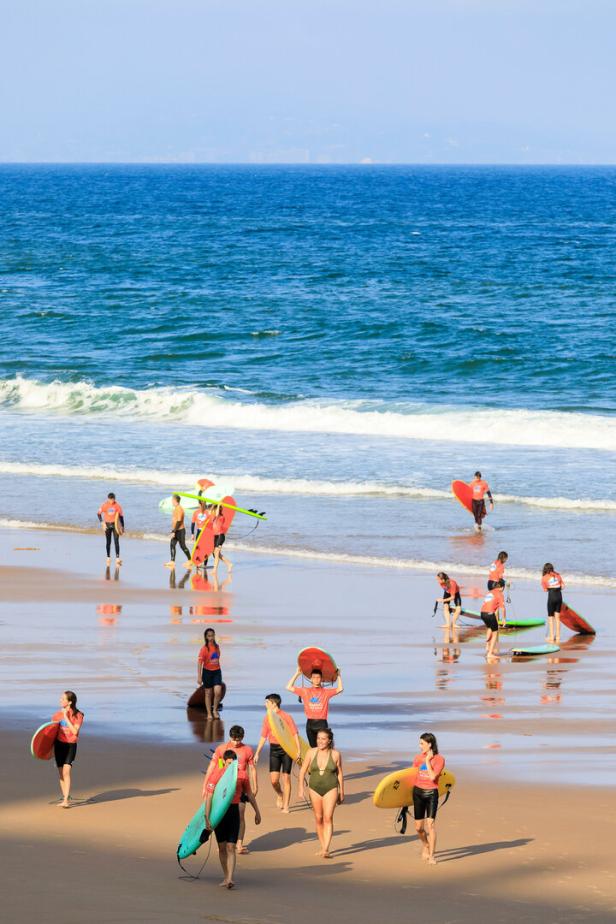 Eine Gruppe von Menschen mit Surfbrettern geht am Strand entlang.