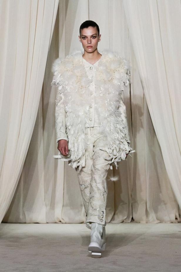Ein Model präsentiert ein weißes Chanel-Ensemble mit Federn auf dem Laufsteg.