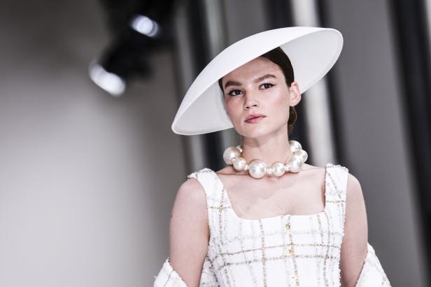 Tamara Ralph präsentiert ein weißes Kleid mit Hut und Perlenkette auf dem Laufsteg der Pariser Fashion Week Haute Couture Herbst/Winter 2025/2026.