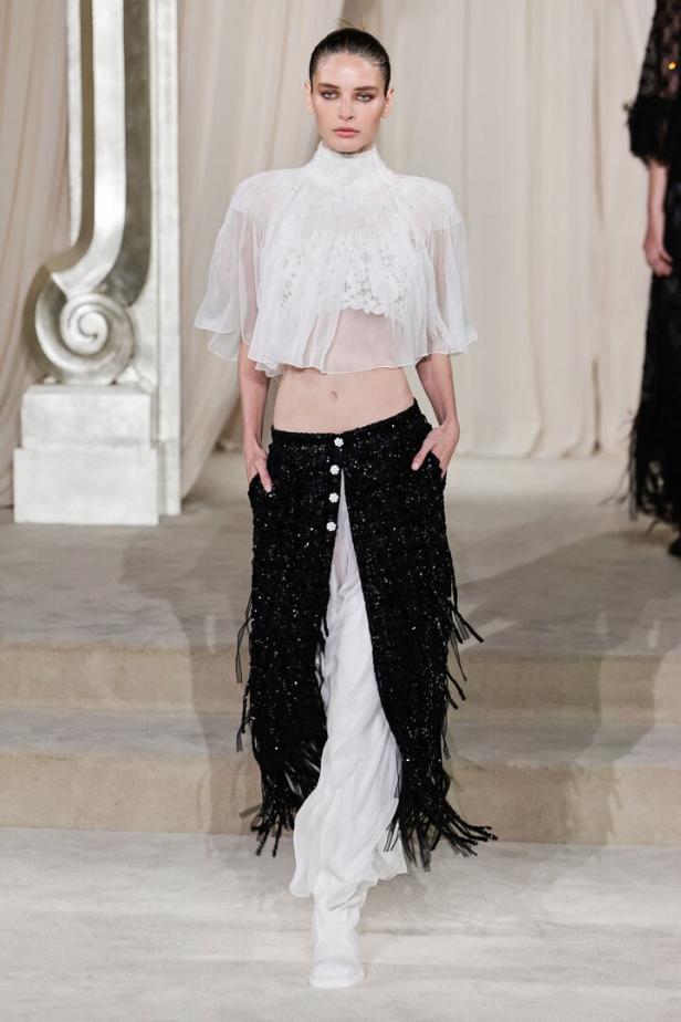 Ein Model präsentiert ein Outfit von Chanel mit einem transparenten Oberteil und einem schwarzen, paillettenbesetzten Rock.