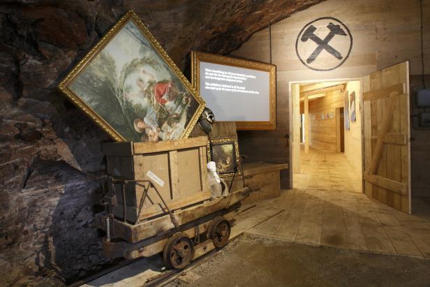 In einem Bergwerk steht ein alter Förderwagen mit Kunstwerken beladen.