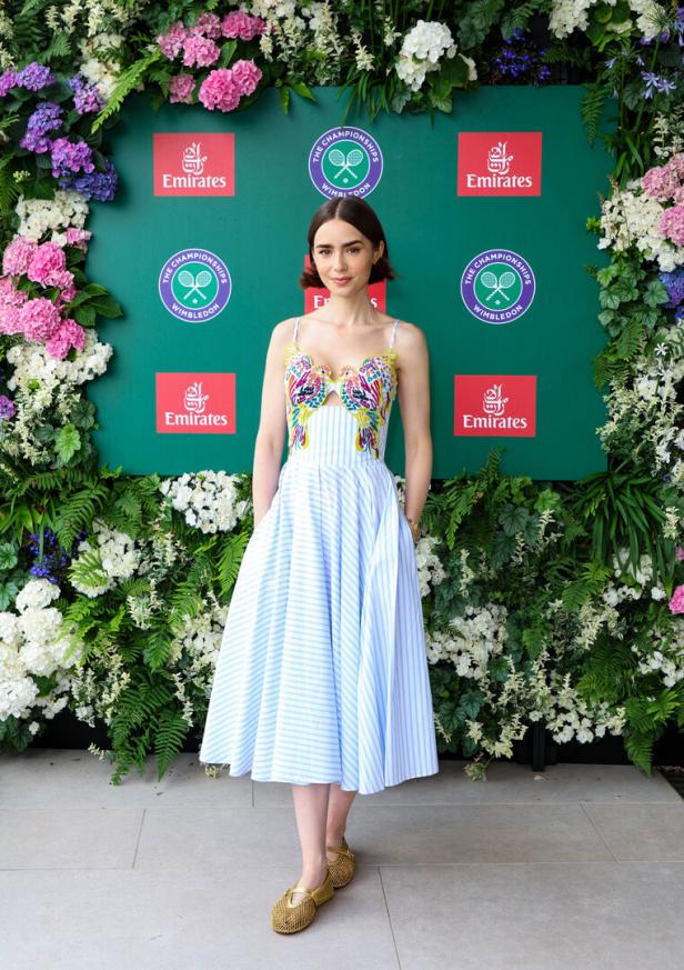 Lily Collins posiert vor einer Wimbledon-Sponsorenwand von Emirates.