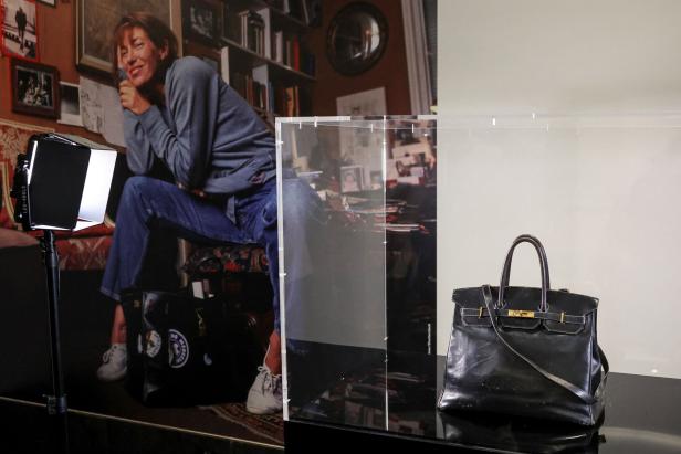 Eine schwarze Birkin Bag steht auf einem Tisch vor einem Foto von Jane Birkin.