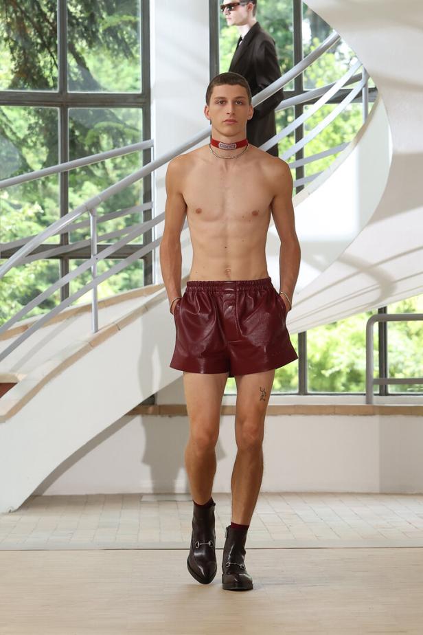 Ein Mann mit freiem Oberkörper trägt Shorts und Stiefel auf einem Laufsteg.