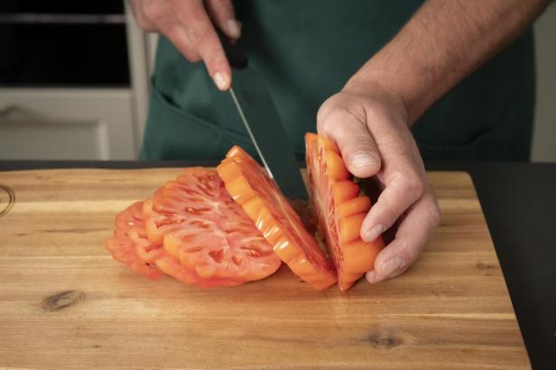Eine Person verwendet ein Schneidebrett, um eine Tomate zu schneiden.