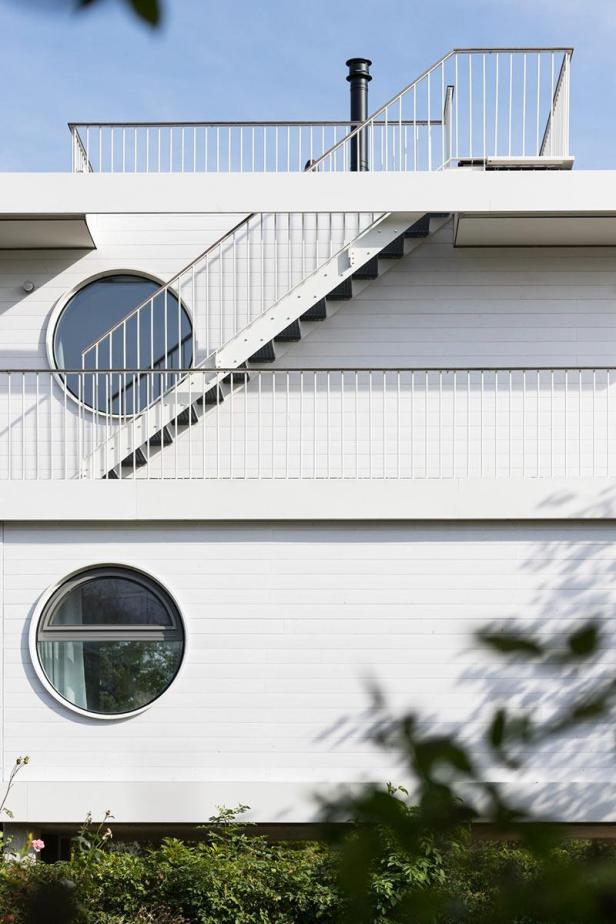 Die Fassade eines weißen Hauses mit runden Fenstern und einer Außentreppe.