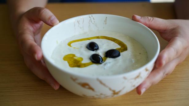Frauenhände halten eine Schüssel, die mit Tzatziki gefüllt ist.
