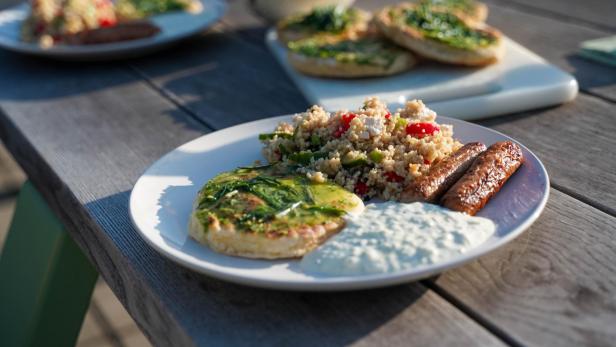 Grillwürstchen, Fladenbrot, Coucous-Salat und Tzatziki sind auf einem Teller angerichtet.