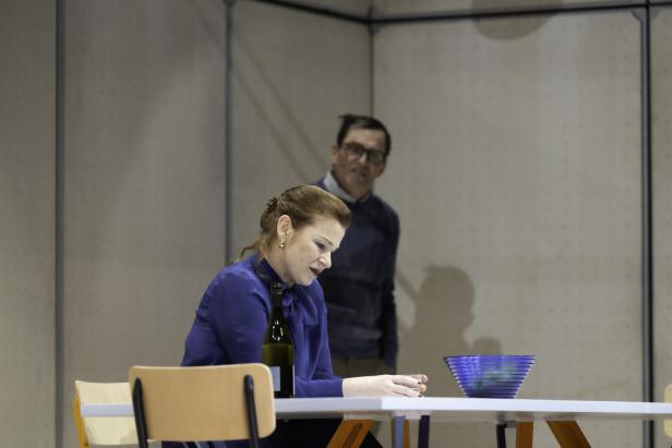 Dörte Lyssewski sitzt an einem Tisch mit einer Flasche Wein und einem Mann im Hintergrund.