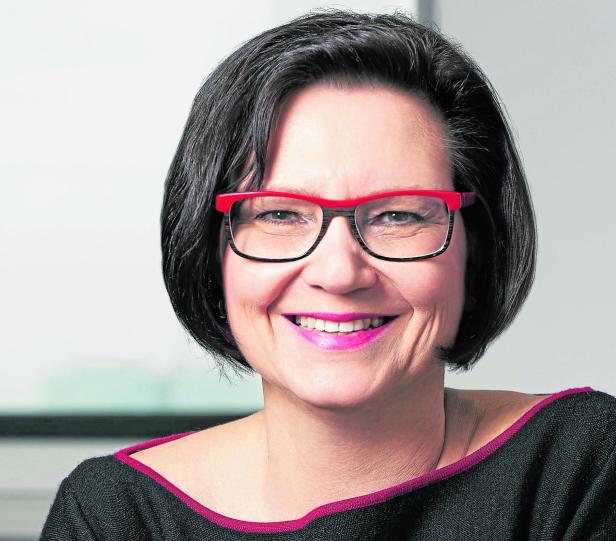 Eine lächelnde Frau mit Brille und dunklen, kurzen Haaren.