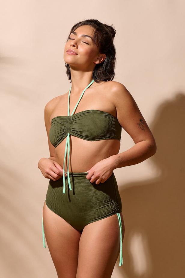 Eine Frau posiert in einem olivgrünen Bikini mit hellgrünen Details.