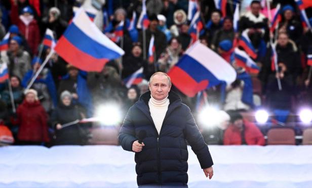 Wladimir Putin bei einer Veranstaltung mit russischen Flaggen im Hintergrund.