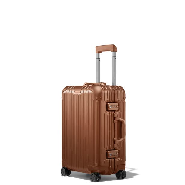 Ein bronzefarbener Rollkoffer mit Teleskopgriff steht auf einem weißen Hintergrund.