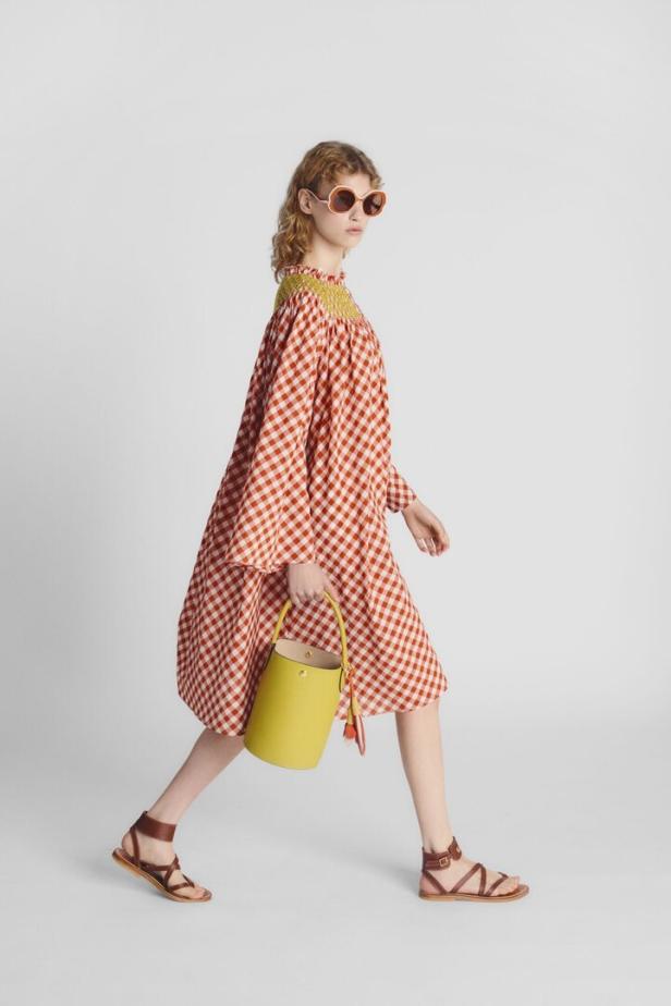Eine Frau mit Sonnenbrille trägt ein rot-weißes Kleid und eine gelbe Handtasche.