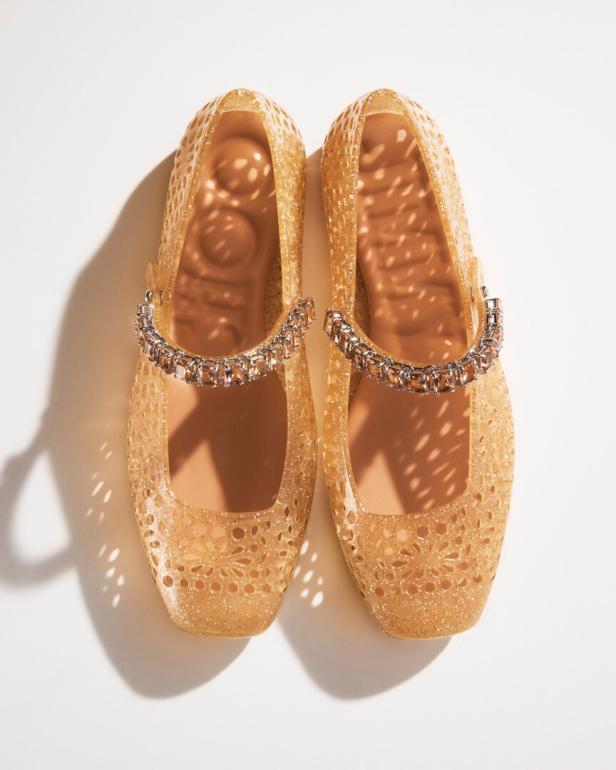 Zwei goldfarbene, durchbrochene Ballerinas mit Schmuckriemchen liegen auf einem weißen Hintergrund.
