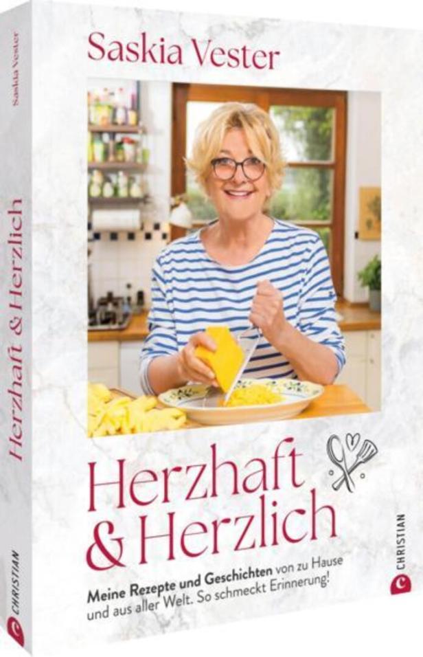 Das Buch „Herzhaft & Herzlich“ von Saskia Vester zeigt die Autorin beim Reiben von Käse.