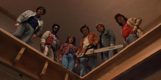 Die Gruppe aus „Stranger Things“ steht mit einer Kettensäge auf einem Dachboden.