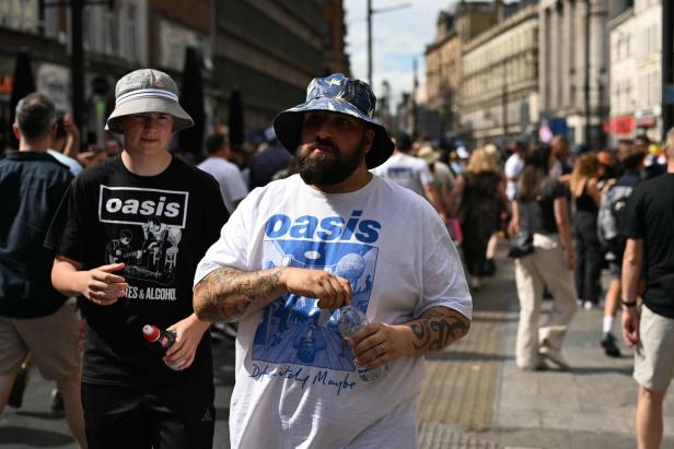 Zwei Männer mit Oasis-T-Shirts gehen eine belebte Straße entlang.