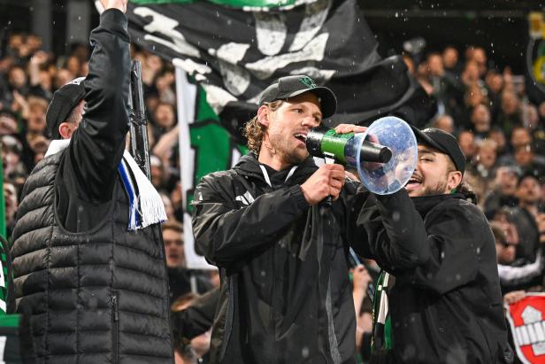 Männer jubeln mit einem Megafon vor einer Menschenmenge, während es regnet.