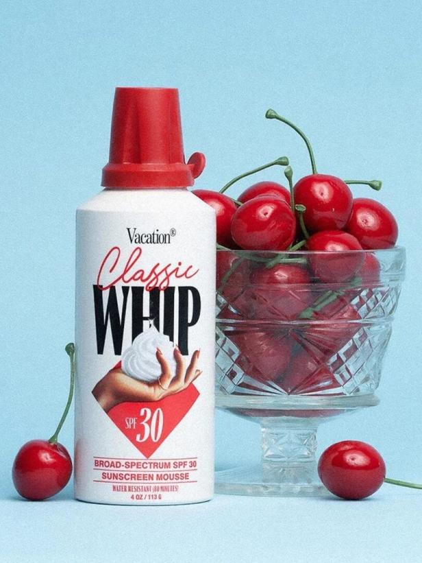 Eine Flasche „Vacation Classic Whip“ Sonnencreme-Mousse neben einer Schale mit Kirschen.