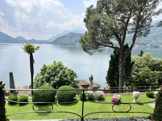Blick von einem Garten auf einen See, umgeben von Bergen.