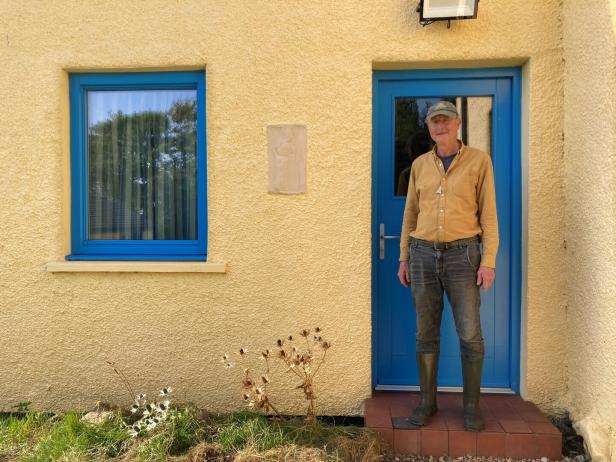 Ein Mann steht vor einer blauen Tür eines gelben Hauses.