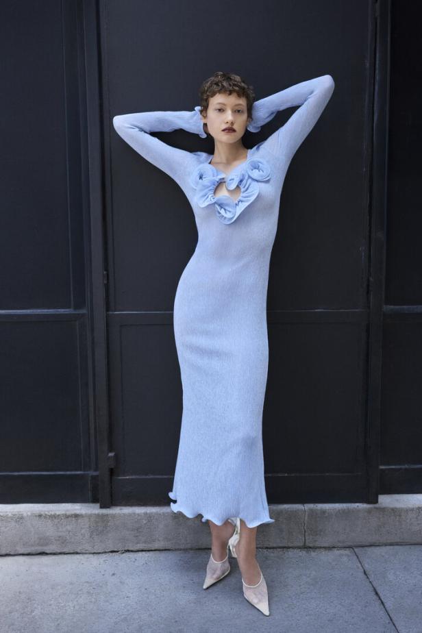 Eine Frau posiert in einem hellblauen, figurbetonten Kleid mit Blumenapplikationen.