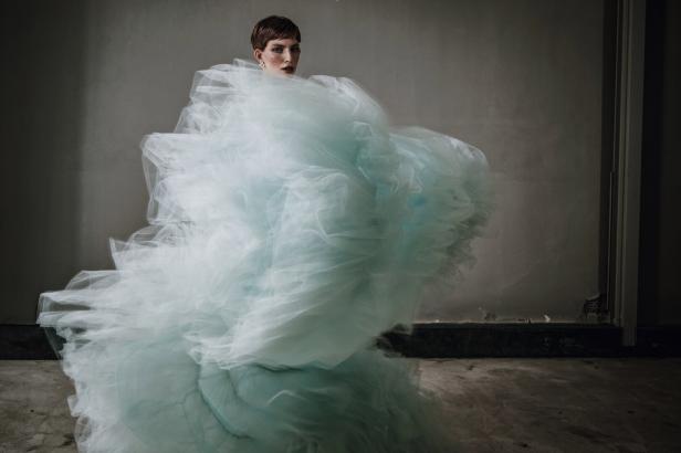 Eine Frau mit kurzen Haaren, gehüllt in ein voluminöses, hellblaues Tüllkleid.