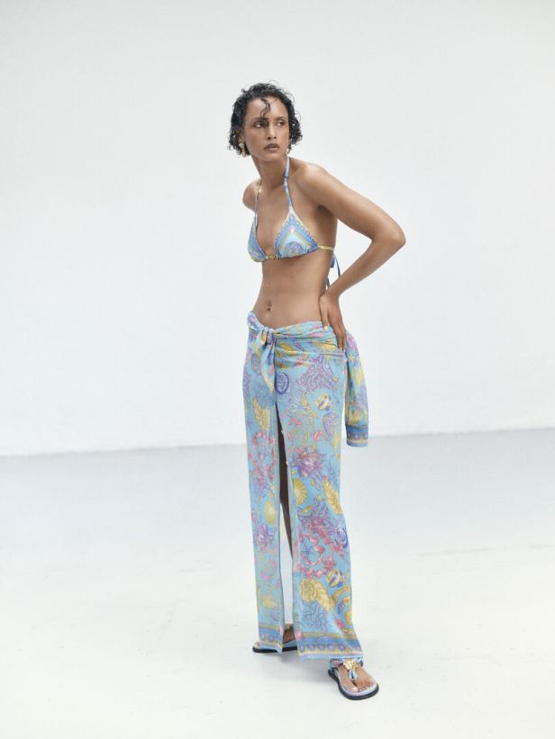 Eine Frau mit dunklen Haaren trägt einen blau gemusterten Bikini und einen passenden Sarong.