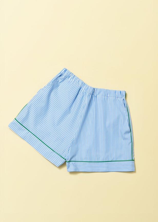 Eine blau-weiß gestreifte Shorts mit grünen Paspeln liegt auf einem hellgelben Hintergrund.