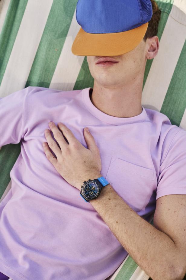 Ein Mann mit Kappe liegt in einer gestreiften Hängematte und trägt eine blaue Armbanduhr.