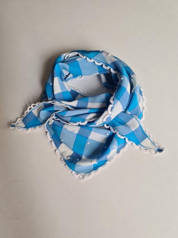 Ein blau-weiß kariertes Halstuch mit gehäkelter Borte liegt auf einem weißen Untergrund.