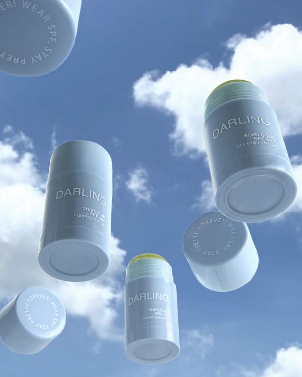 Mehrere „Darling Shield-Me SPF 50+ Clear Sun Stick“-Sonnenstifte vor blauem Himmel.