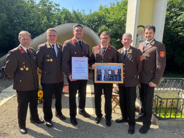 Eine Gruppe von Feuerwehrleuten in Uniform posiert mit einer Urkunde und einem gerahmten Foto.