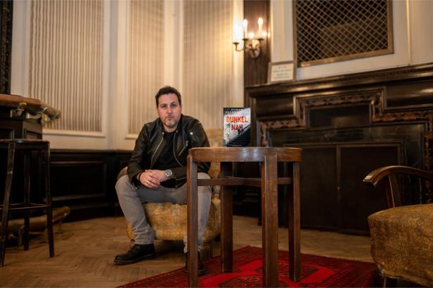 Ein Mann sitzt in einem Sessel, im Vordergrund steht das Buch „Dunkel Nah“.