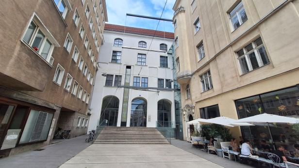 Blick in eine Gasse mit einem Gebäude mit Treppe und einem Café.