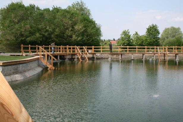 Zwei Personen stehen auf einer Holzbrücke, die über einen kleinen See führt.