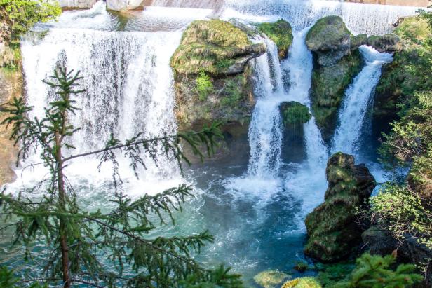 Ein mehrstufiger Wasserfall stürzt über bemooste Felsen in einen türkisfarbenen See.