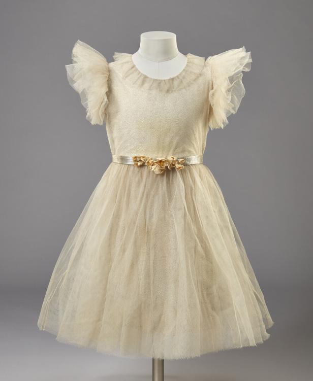Ein beigefarbenes Kleid mit Tüllrock und Blumenapplikation auf einem Schneiderbüste.