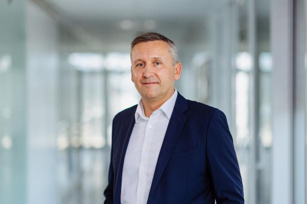 Ein Mann in einem blauen Anzug und einem weißen Hemd lächelt in die Kamera.